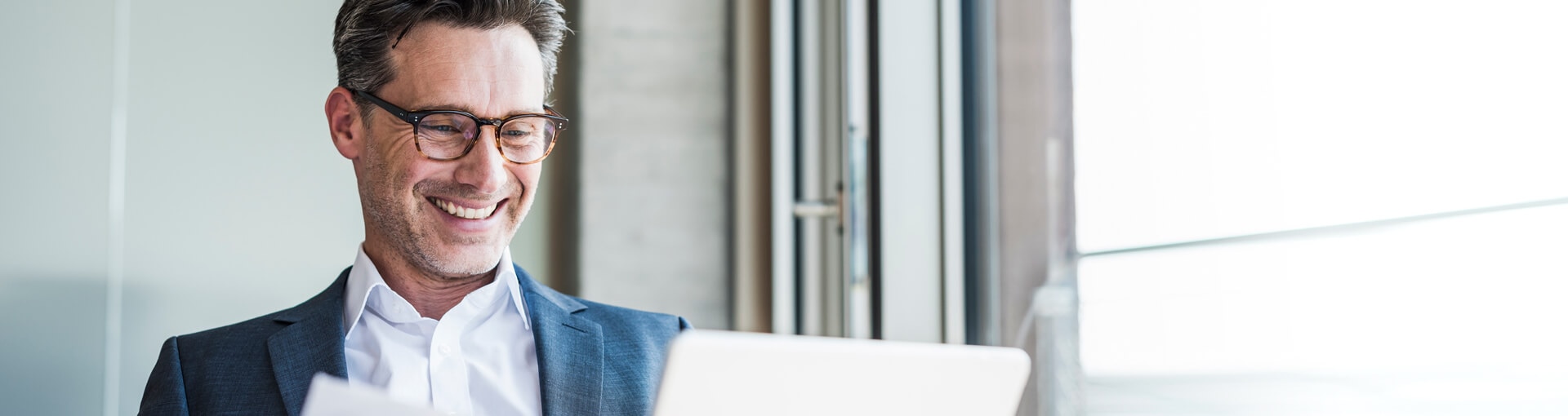 Businessman with glasses smiling and using a laptop.