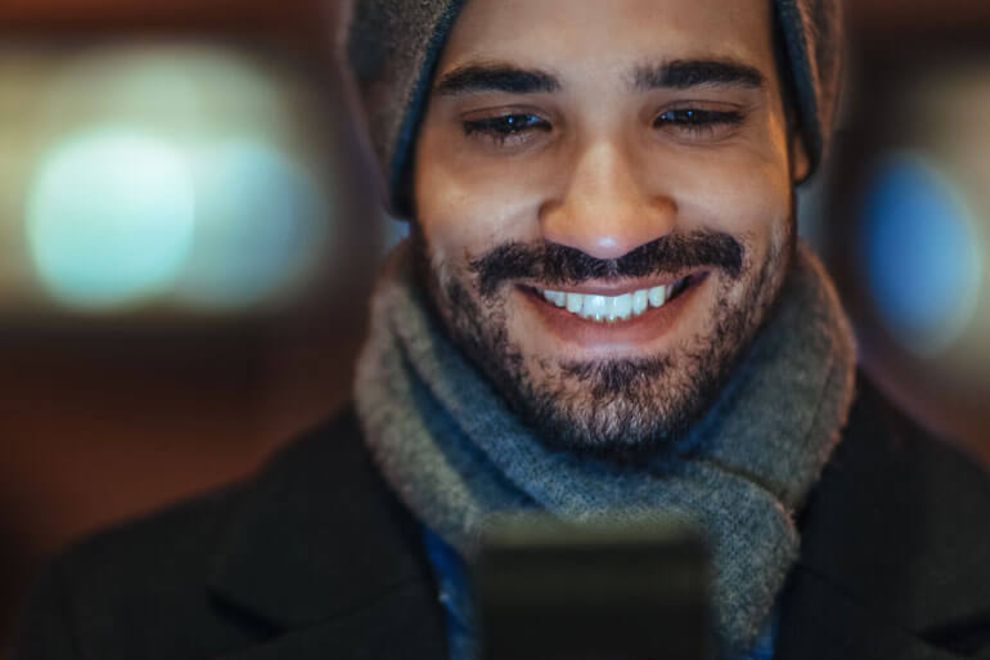 Young man in winter attire uses a smartphone.