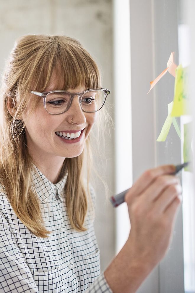 Young woman with glasses writing on a post-it note.