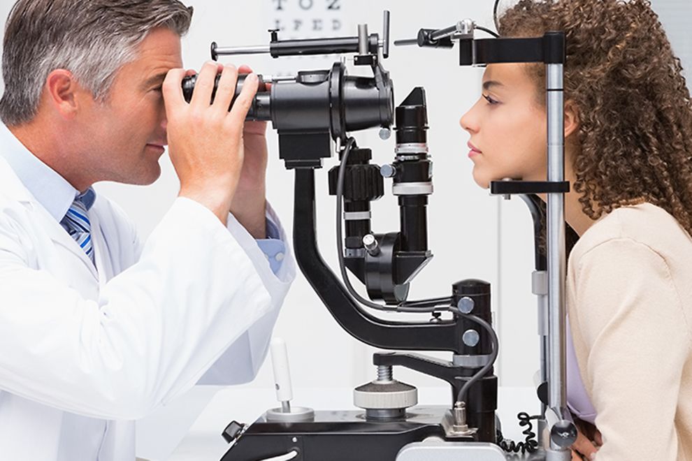An eye doctor performs an eye exam on a young woman