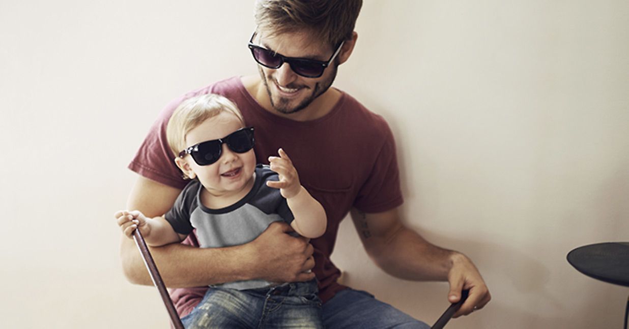 father holding toddler son on his lap, both of them are wearing sunglasses